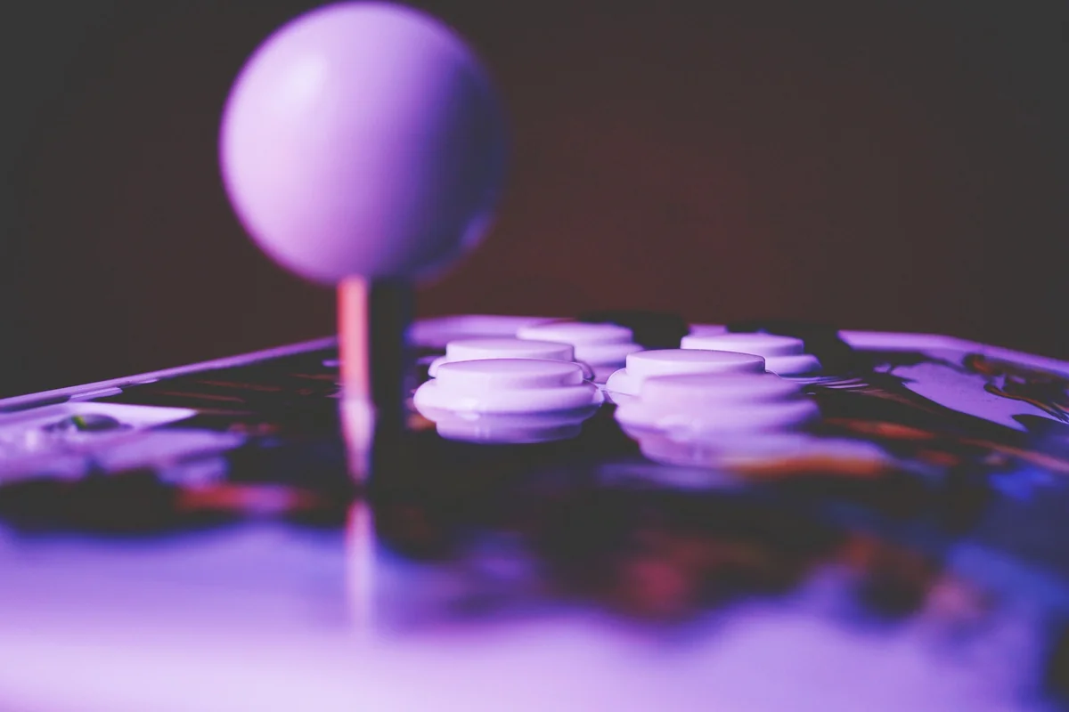 Arcade-style fight stick with a white ball-top joystick and push buttons under purple lighting