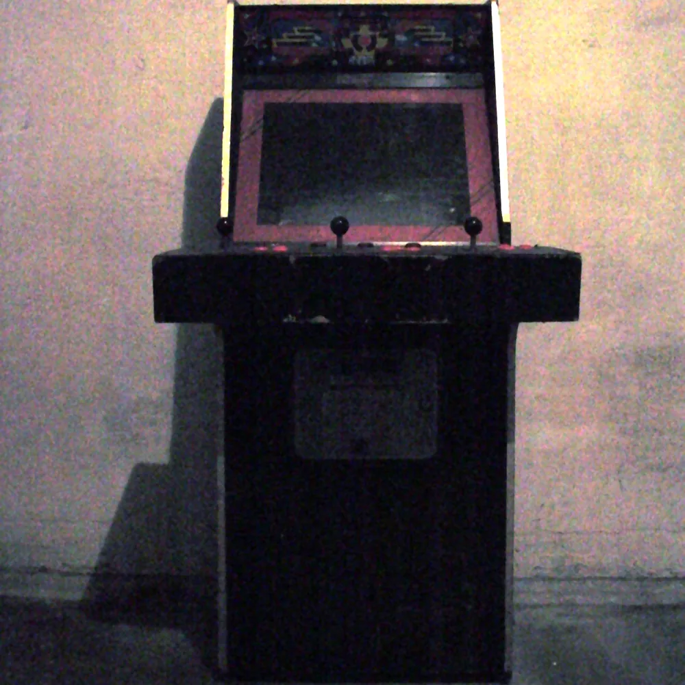 Upright wooden arcade cabinet with joysticks on its control panel, standing against a plain wall